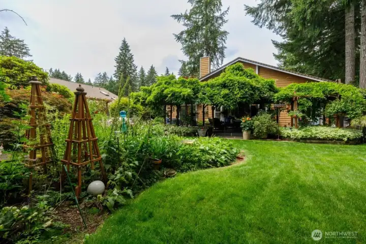 A shot of the home from the backyard - you can see the beautifully kept lawn, garden space, deck, and the back of the home.