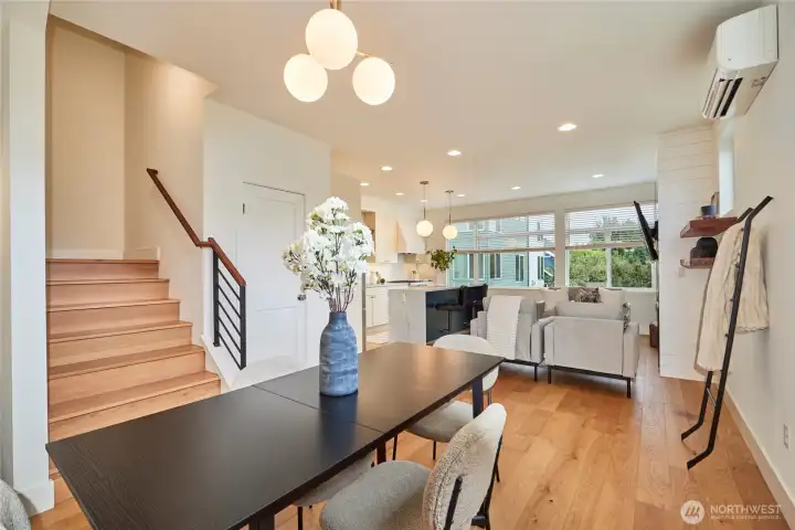 A look from the dining area to the living room and kitchen. Note the oak hardwoods, ductless split heat/AC, wall of windows and designer finishes.