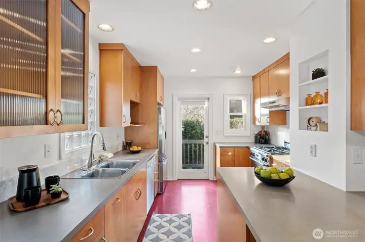 Full of natural light and classic charm, the kitchen features  Marmoleum flooring, glass-fronted cabinets, and both a leaded glass door to the dining room  and a glass-paned door to the backyard. Modern updates include a Bosch dishwasher, Fisher &  Paykel fridge, Décor gas range, and Allure hood vent. Step right out to the back deck and  tiered yard—perfect for morning coffee or summer dinners al fresco.