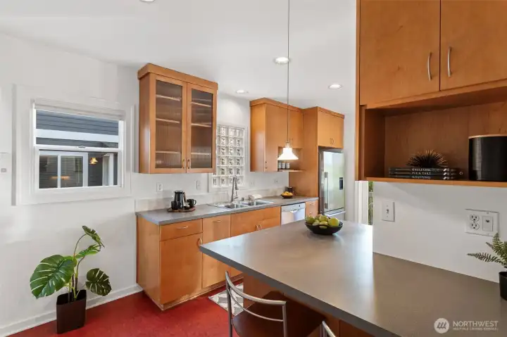 Full of natural light and classic charm, the kitchen features  Marmoleum flooring, glass-fronted cabinets, and both a leaded glass door to the dining room  and a glass-paned door to the backyard. Modern updates include a Bosch dishwasher, Fisher &  Paykel fridge, Décor gas range, and Allure hood vent. Step right out to the back deck and  tiered yard—perfect for morning coffee or summer dinners al fresco.