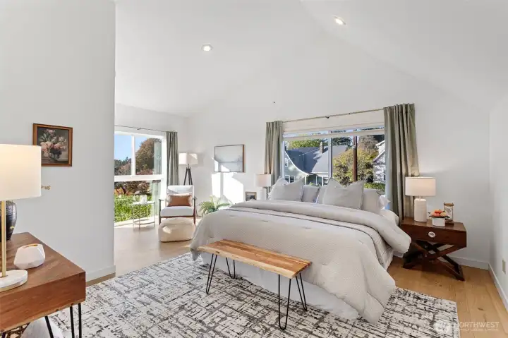 The primary bedroom on the upper level with cathedral ceilings and large new windows frame views of downtown and the evening sky, filling the room with golden light. From sunrise to sunset, it’s a peaceful retreat  that feels timeless— high above the tiered gardens below.