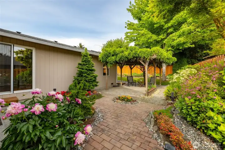 A view of the side yard, with the slider from the primary suite visible at far left.  Wisteria covered patio provides shade, color, and an intimate space for relaxation.