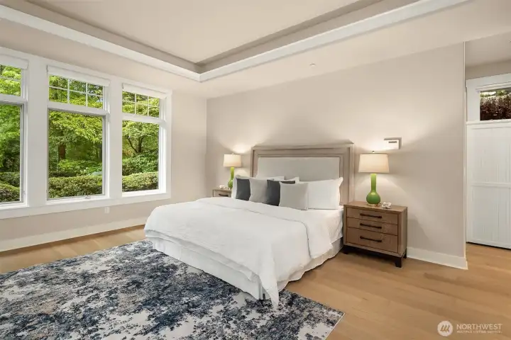 The main-level primary suite is a serene retreat, featuring new European white oak engineered floors, tray ceiling, and tranquil green outlooks - and the convenience of washer/dryer hookups within the suite.