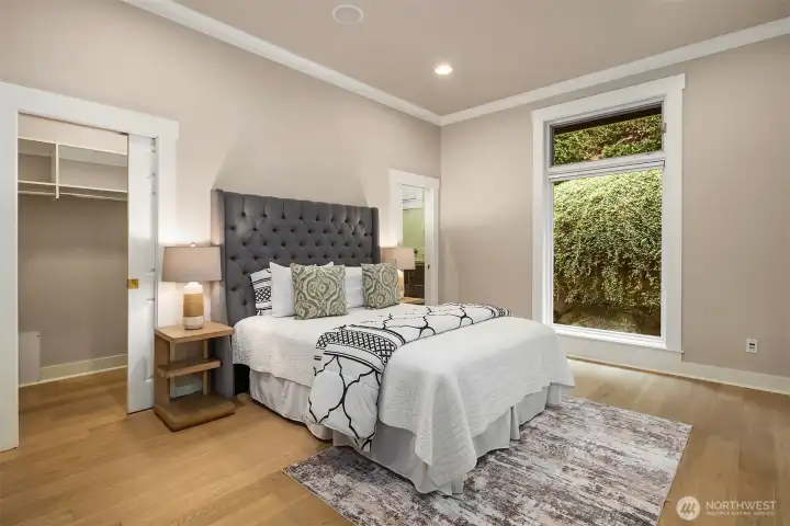 The main-level junior suite offers a peaceful retreat with large windows, new European engineered white oak floors, a walk-in closet, and direct access to the private covered patio.