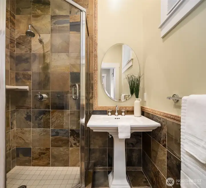 The junior three-quarter bath is appointed with rich slate tile, a pedestal sink, and a walk-in shower - a perfectly curated space.