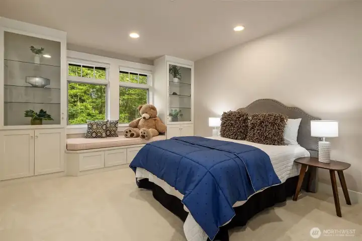 A generously sized upper bedroom features new carpet, large windows with a built-in window seat, custom curio cabinet storage, and a walk-in closet that goes well beyond the expected.