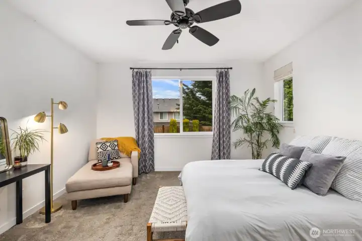 Alternate view of the bedroom highlighting multiple windows, ceiling fan, and relaxing seating corner positioned to enjoy the outdoor greenery.