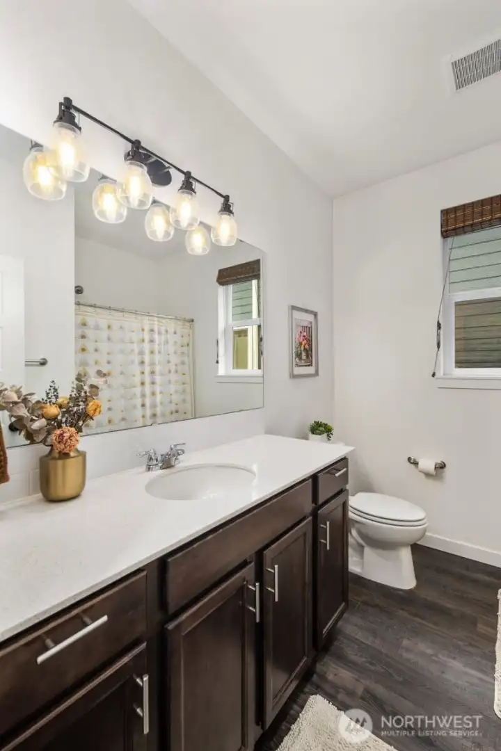 Another view of the bathroom highlighting the long vanity counter, warm wood cabinetry, and bright mirror lighting that makes the room feel open and welcoming.