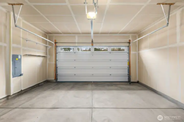 Spacious attached two-car garage with overhead door, built-in shelving for storage, and room for vehicles, tools, or outdoor gear.