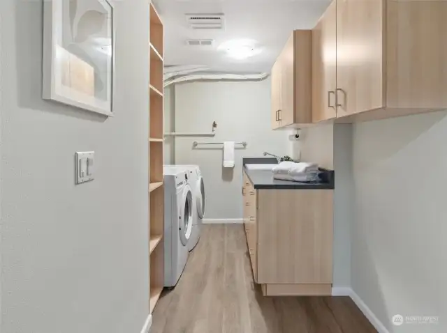 A spacious laundry room beautifully appointed with custom cabinetry, a convenient sink, and ample shelving for optimal organization.