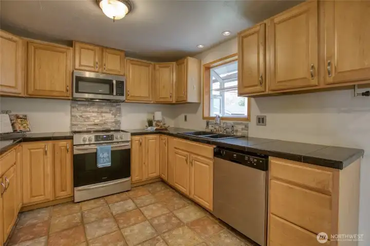 Warm wood cabinetry, stainless appliances, travertine tile flooring & a garden window give the kitchen a comfortable feel that invites you to slow down and stay awhile.