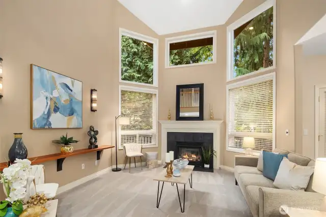 Stunning living room with soaring 16ft ceiling, floor to ceiling windows, and a cozy fireplace that provides added warmth.