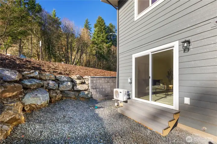 Ground-level outdoor area with retaining wall and natural surroundings, offering functional exterior space for this Friday Harbor townhome.