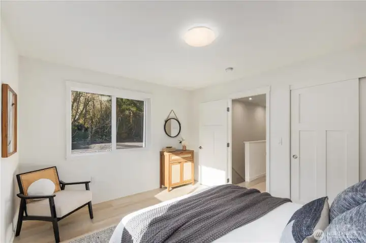 Light-filled upstairs bedroom featuring large window, neutral finishes, and modern new-construction design in this Friday Harbor townhome.