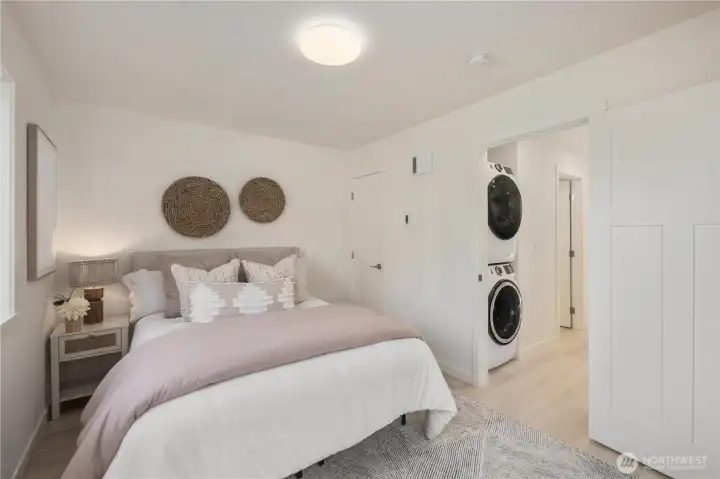 Upper-level bedroom featuring neutral finishes, modern design, and convenient access to in-unit stacked washer and dryer, offering functional living in this newly constructed Friday Harbor townhome.
