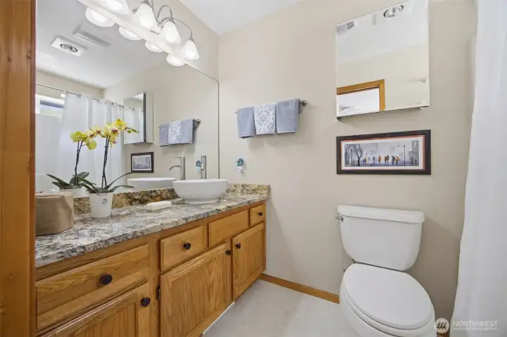 There is a large vanity in the primary full bathroom that has a unique vessel sink and lots of counter space and storage in the oak cabinets and drawers.
