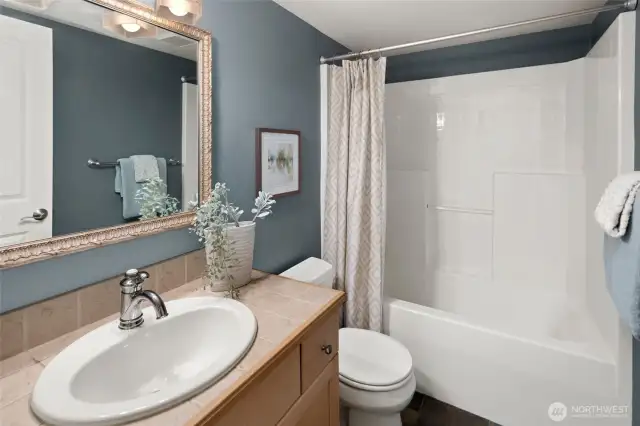 The lower-level full bathroom showcases soft blue walls, natural stone tile, and a tub/shower combo—blending bold design with everyday function.