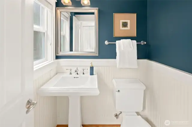 A handsome powder room on the main floor features crisp wainscoting, a pedestal sink, and elegant lighting—perfect for guests.