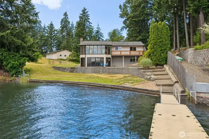 Standing on the private dock and looking back toward the home, you can appreciate the full breadth of the 88 feet of shoreline and the thoughtful way the property unfolds from the water's edge. Wide terraced steps gently transition from the lake to the expansive upper lawn, creating easy access while adding visual interest to the landscape. Mature trees frame the perimeter of the property, providing privacy without sacrificing sunlight or views, while the home enjoys a wonderfully open setting overlooking the water. In the distance, you can even spot the detached shop perched above, highlighting the impressive scale and versatility of this unique lakefront property. Standing on the private dock and looking back toward the home, you can appreciate the full breadth of the 88 feet of shoreline and the thoughtful way the property unfolds from the water's edge. Wide terraced steps gently transition from the lake to the expansive upper lawn, creating easy access while adding visual interest to the landscape. Mature trees frame the perimeter of the property, providing privacy without sacrificing sunlight or views, while the home enjoys a wonderfully open setting overlooking the water. In the distance, you can even spot the detached shop perched above, highlighting the impressive scale and versatility of this unique lakefront property.