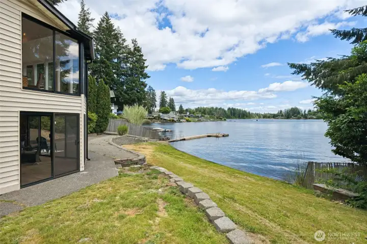 Here you can see the full 88 feet of Long Lake frontage stretching across the property, along with the private dock waiting for summer adventures. The side of the home is lined with large windows designed to capture water views and natural light, while attractive hardscaping creates an easy pathway leading from the front of the home to the backyard patio, lawn and shoreline beyond. Whether you're carrying paddleboards to the water, heading out for an evening boat ride or simply taking a sunset stroll along your own waterfront, everything about this layout encourages you to spend more time outside enjoying the lake. Here you can see the full 88 feet of Long Lake frontage stretching across the property, along with the private dock waiting for summer adventures. The side of the home is lined with large windows designed to capture water views and natural light, while attractive hardscaping creates an easy pathway leading from the front of the home to the backyard patio, lawn and shoreline beyond. Whether you're carrying paddleboards to the water, heading out for an evening boat ride or simply taking a sunset stroll along your own waterfront, everything about this layout encourages you to spend more time outside enjoying the lake.