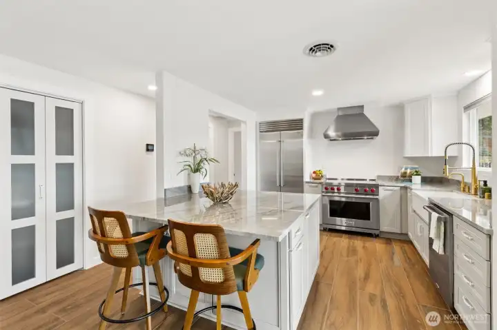 Now we're getting to one of the crown jewels of the renovation. This beautifully remodeled kitchen pairs timeless design with serious appliance muscle, featuring approximately $40,000 in premium upgrades including a Wolf electric cooktop, double ovens, dishwasher, microwave and refrigerator. Crisp white shaker cabinetry and stunning white quartz countertops create a bright, airy atmosphere, while the warm luxury vinyl plank flooring flows seamlessly from the adjoining living spaces for a cohesive feel throughout the main floor. The island offers comfortable seating for casual meals, conversation or keeping the cook company, and the nearby pantry provides convenient storage just steps away. Now we're getting to one of the crown jewels of the renovation. This beautifully remodeled kitchen pairs timeless design with serious appliance muscle, featuring approximately $40,000 in premium upgrades including a Wolf electric cooktop, double ovens, dishwasher, microwave and refrigerator. Crisp white shaker cabinetry and stunning white quartz countertops create a bright, airy atmosphere, while the warm luxury vinyl plank flooring flows seamlessly from the adjoining living spaces for a cohesive feel throughout the main floor. The island offers comfortable seating for casual meals, conversation or keeping the cook company, and the nearby pantry provides convenient storage just steps away.