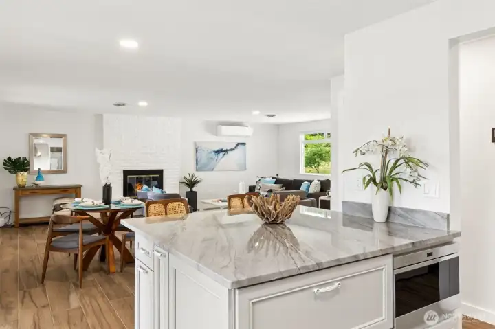 This perspective perfectly captures how the kitchen serves as the heart of the home while remaining connected to everything happening around it. The expansive quartz island showcases beautiful white surfaces accented by soft gray veining, creating a timeless look that feels both elegant and approachable. Built-in appliances, including the integrated microwave, help maintain the clean lines of the design, while the classic white shaker cabinetry ensures the space will remain stylish for years to come. From the island, you can chat with guests gathered in the dining room, enjoy views of the dramatic floor-to-ceiling brick fireplace in the living room or simply glance toward the lake and watch the water sparkle beyond. This perspective perfectly captures how the kitchen serves as the heart of the home while remaining connected to everything happening around it. The expansive quartz island showcases beautiful white surfaces accented by soft gray veining, creating a timeless look that feels both elegant and approachable. Built-in appliances, including the integrated microwave, help maintain the clean lines of the design, while the classic white shaker cabinetry ensures the space will remain stylish for years to come. From the island, you can chat with guests gathered in the dining room, enjoy views of the dramatic floor-to-ceiling brick fireplace in the living room or simply glance toward the lake and watch the water sparkle beyond.