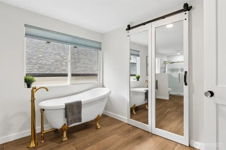 The mirrored barn-door-style closet doors add character while helping bounce natural light throughout the room, and they create a stylish entrance to the walk-in closet beyond. Front and center is the gorgeous freestanding clawfoot soaking tub paired with an eye-catching floor-mounted filler that gives the space a distinctly upscale feel. In the mirror's reflection, you can see the walk-in shower waiting just beyond, completing a layout that feels remarkably spa-like without sacrificing functionality. The mirrored barn-door-style closet doors add character while helping bounce natural light throughout the room, and they create a stylish entrance to the walk-in closet beyond. Front and center is the gorgeous freestanding clawfoot soaking tub paired with an eye-catching floor-mounted filler that gives the space a distinctly upscale feel. In the mirror's reflection, you can see the walk-in shower waiting just beyond, completing a layout that feels remarkably spa-like without sacrificing functionality.