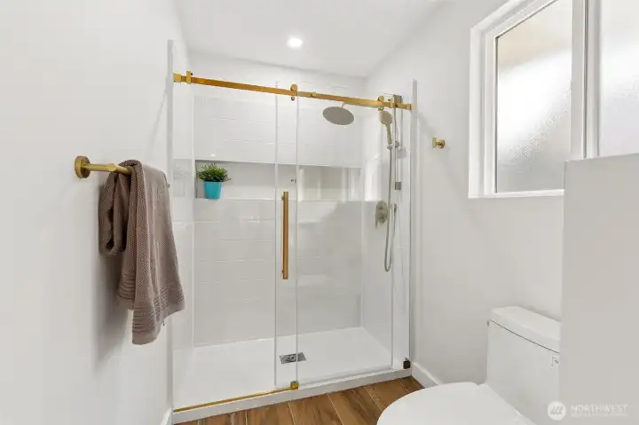 Tile surrounds the shower for a clean, timeless look, while the brushed gold fixtures add warmth and just the right amount of luxury. The glass enclosure keeps the space feeling open and bright, and the nearby toilet is thoughtfully positioned beneath a privacy-glass window that welcomes natural light while maintaining seclusion. Open the window for a little fresh lake air and enjoy a bathroom that feels more like a boutique spa than a typical primary suite bath. Tile surrounds the shower for a clean, timeless look, while the brushed gold fixtures add warmth and just the right amount of luxury. The glass enclosure keeps the space feeling open and bright, and the nearby toilet is thoughtfully positioned beneath a privacy-glass window that welcomes natural light while maintaining seclusion. Open the window for a little fresh lake air and enjoy a bathroom that feels more like a boutique spa than a typical primary suite bath.