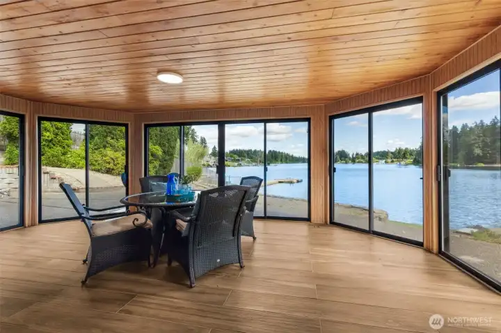 This spectacular lake-facing room is one of the most unique spaces in the home. Designed with a graceful curved wall that reaches out toward the water, it captures panoramic views of Long Lake and creates a front-row seat to every sunrise, season and waterfront activity. Warm wood-plank ceilings add character overhead while waterproof luxury vinyl plank flooring keeps the space both beautiful and practical for everyday lake living. Multiple sliding glass doors invite fresh breezes inside and allow the room to flow effortlessly onto the outdoor entertaining areas. Whether you're hosting friends, enjoying morning coffee or simply watching the light dance across the water, this room delivers the kind of view most people only experience on vacation. This spectacular lake-facing room is one of the most unique spaces in the home. Designed with a graceful curved wall that reaches out toward the water, it captures panoramic views of Long Lake and creates a front-row seat to every sunrise, season and waterfront activity. Warm wood-plank ceilings add character overhead while waterproof luxury vinyl plank flooring keeps the space both beautiful and practical for everyday lake living. Multiple sliding glass doors invite fresh breezes inside and allow the room to flow effortlessly onto the outdoor entertaining areas. Whether you're hosting friends, enjoying morning coffee or simply watching the light dance across the water, this room delivers the kind of view most people only experience on vacation.