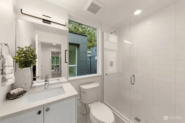 A bathroom that balances modern style with natural touches. Notice the oversized glass shower with sleek tiling and the large window flooding the space with light—a serene retreat to start and end your day