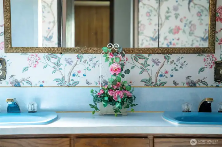 The iconic blue bathroom is full of personality, complete with double sinks, coordinating counters, floral wallpaper, and a gold tri-fold mirror. The iconic blue bathroom is full of personality, complete with double sinks, coordinating counters, floral wallpaper, and a gold tri-fold mirror.
