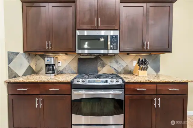 The stone backsplash looks sharp against the stainless steel microwave and propane stove
