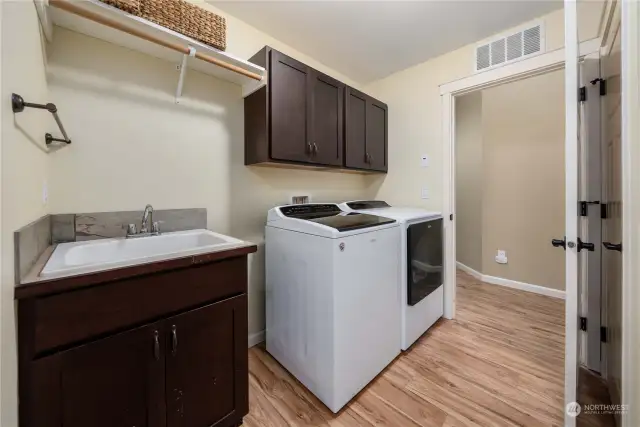 Laundry room off main hallway features convenient sink, storage closet, cabinets and clothes rod. This also leads to bonus room stair access