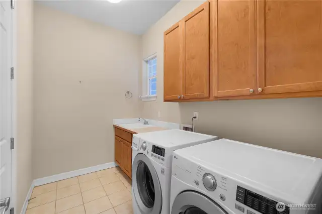 Laundry room with upgraded cabinets, sink, and tile floors.