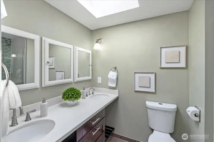 Primary en-suite bathroom with dual sinks, walk-in shower, quartz counter tops & a skylight
