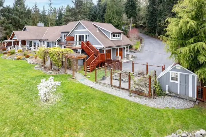 A look at the home and driveway access to the 2-car garage. A fenced vegetable garden and garden shed are in the foreground.