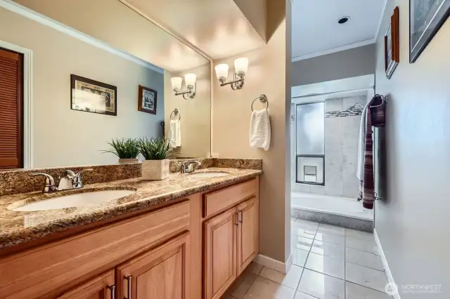 The en-suite Primary bathroom boasts travertine tile floors, a dual vanity with a striking slab granite counter, and a soaking tub/shower combo for ultimate relaxation.