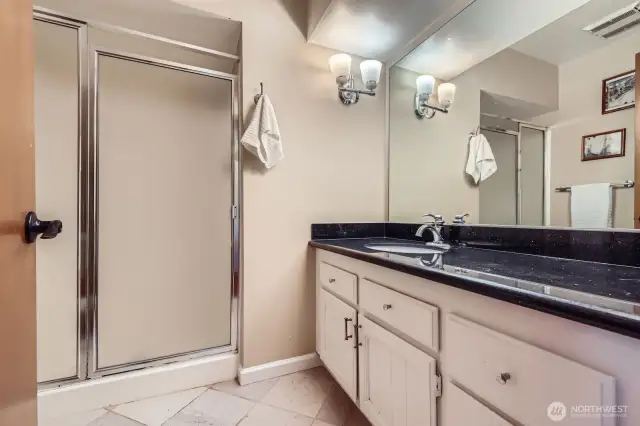 Dressed to impress, the ¾ hall bathroom has a stylish black slab granite counter, white vanity, and grey & white travertine tile floors.
