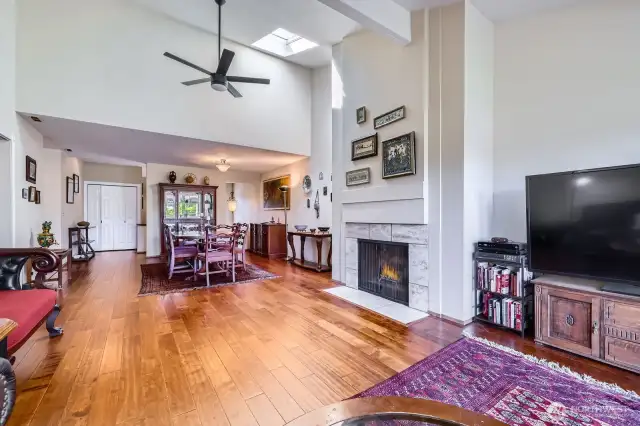 The open-concept living and dining spaces feature a stately travertine-surround fireplace, skylight, and a modern fan.