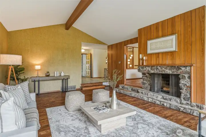 Looking to the entry, dining room behind the fireplace. Refinished hardwoods, grasscloth wallpaper, wood paneling, and a striking stone fireplace. Midcentury character beautifully preserved