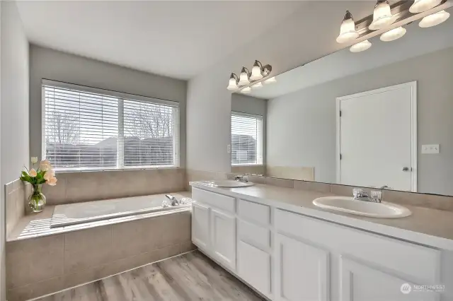 The spacious primary bathroom boasts an expansive 5-piece bath, featuring freshly painted cabinetry and brand-new luxury vinyl plank flooring. With dual sinks, a large walk-in closet, and a luxurious soaking tub, offering a serene and indulgent retreat.