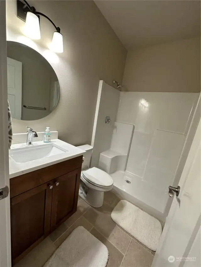 Lower level bathroom with large step in shower, tile flooring, solid surface counter with undermounted sink.