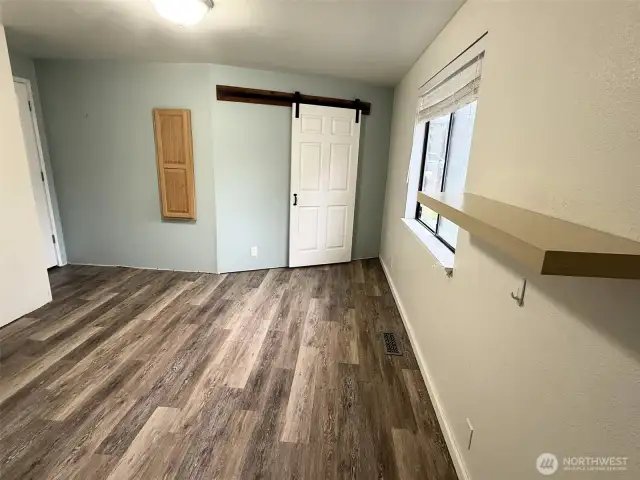 Main level bedroom with a barn door leading into the closet, and a fold out ironing board cabinet.