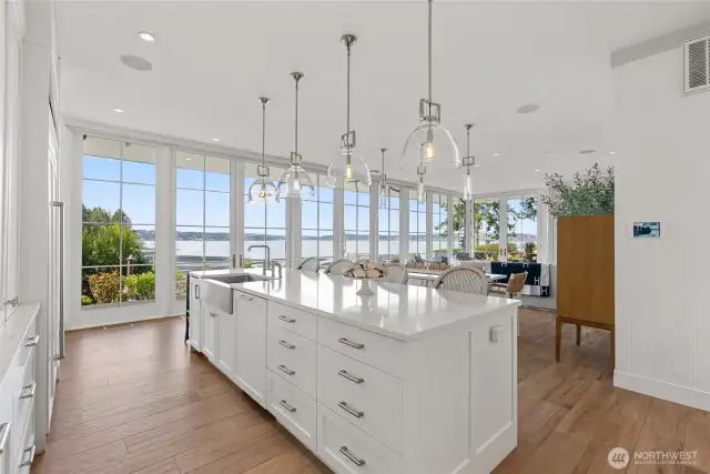Anchored by quartz counters and custom cabinetry, the kitchen shines with pendant lighting, ample storage, and high-end appliances—Sub-Zero, Bosch, and GE nugget ice maker. From the breakfast counter, the view stretches through the dining room to curated gardens and the water beyond.