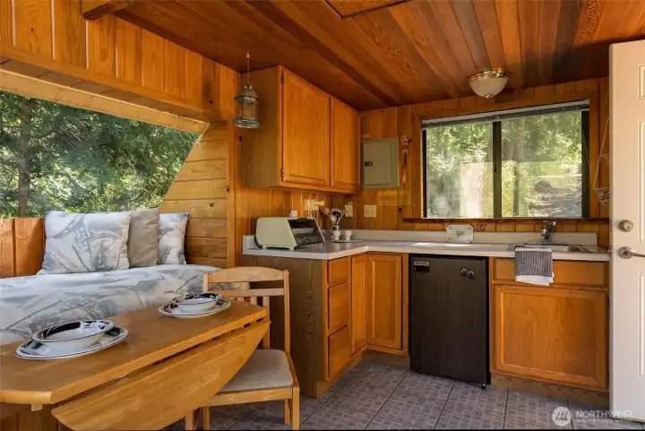 Rustic cabin interior offers meal prep space, sink, fridge, storage and plenty of natural light.
