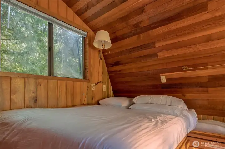 Loft bedroom wrapped in wood-clad walls and a window that brings the outdoors in.