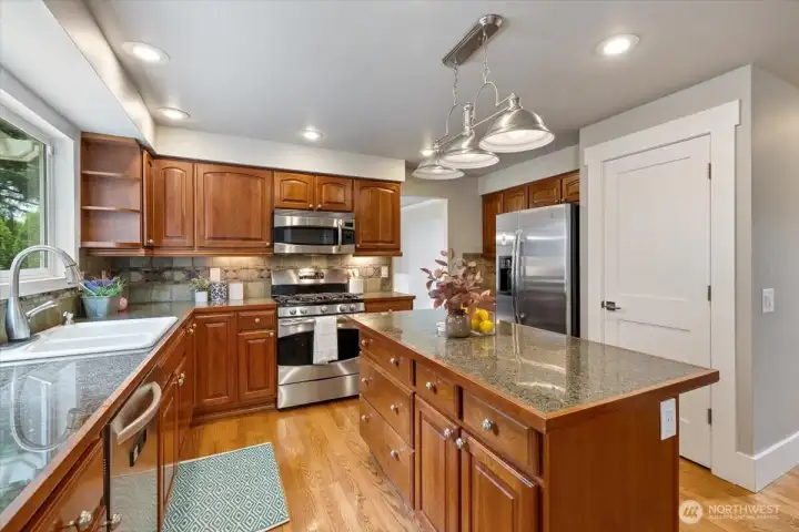 Warm kitchen cabinetry with pull-outs and island. Tile backsplash and granite tile counters.