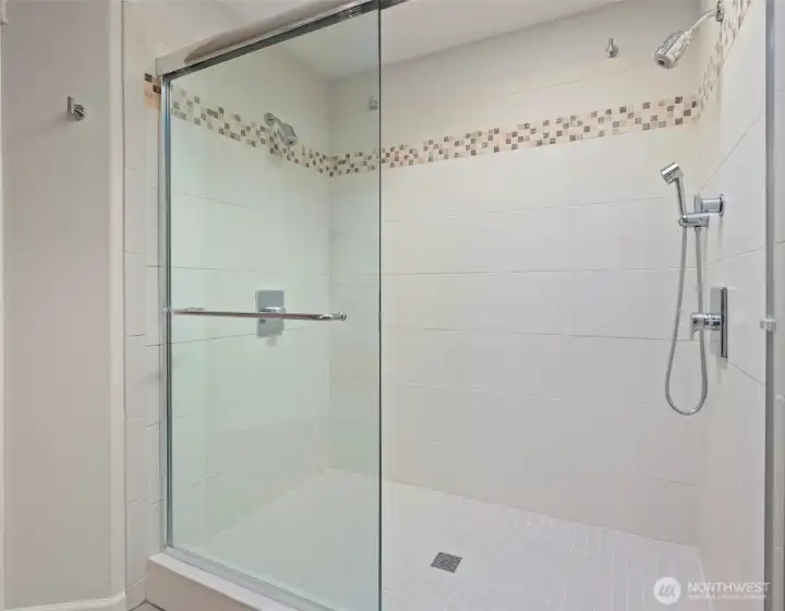 Large dual-control tiled shower with heavy-duty glass shower door with anti-scale coating for easy maintenance.