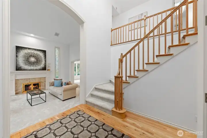 Bright, welcoming foyer featuring hardwood floors, soaring ceilings, and a classic wood staircase—creating a grand yet inviting first impression.