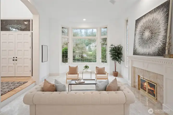 A stunning view of the living room showcasing the gas fireplace, bay-style windows overlooking lush greenery, and an open flow to adjacent living spaces.
